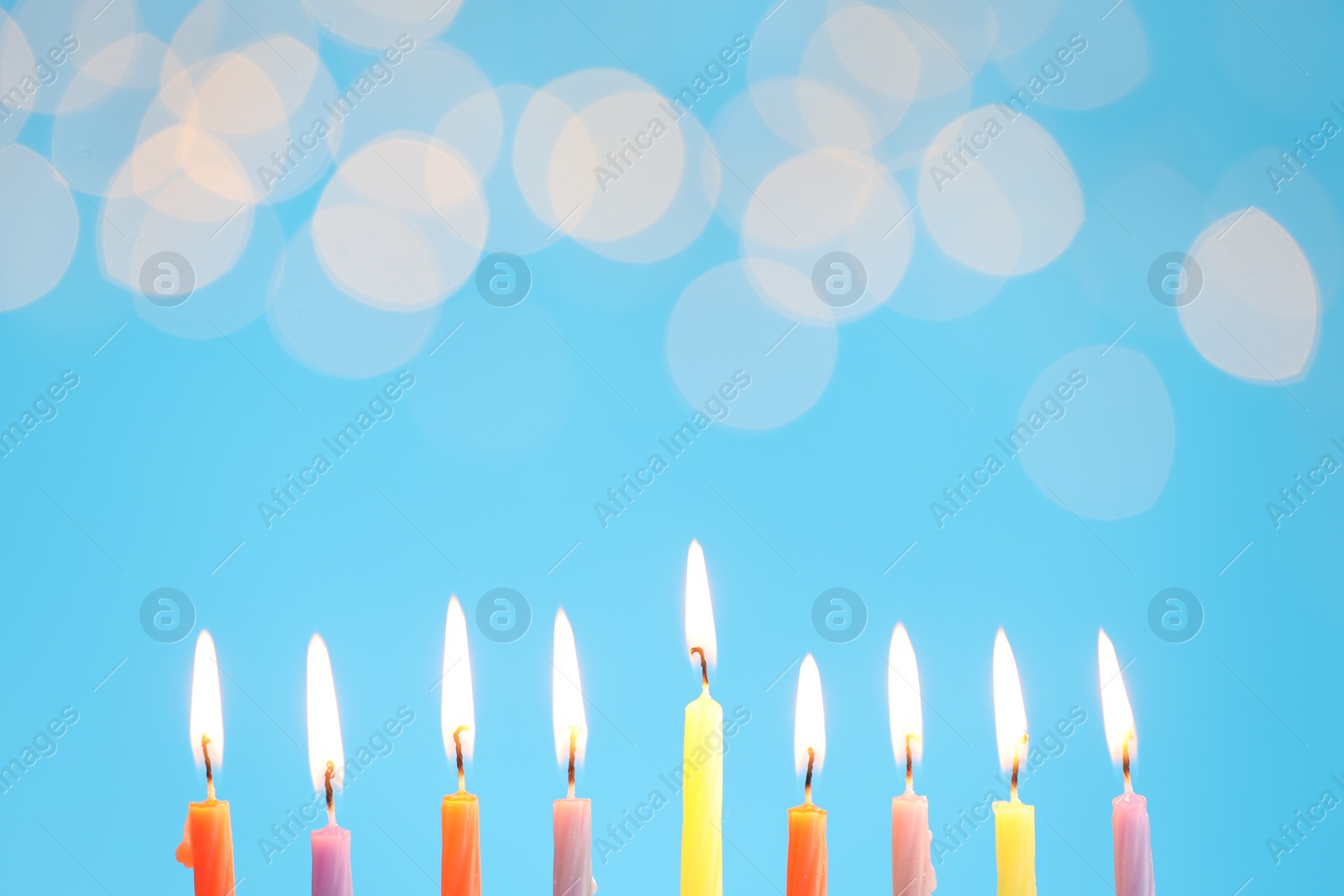Photo of Hanukkah celebration. Burning candles on light blue background with blurred lights, space for text