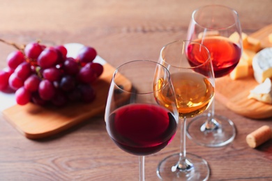 Photo of Glasses with different wines and appetizers on wooden table, closeup. Space for text