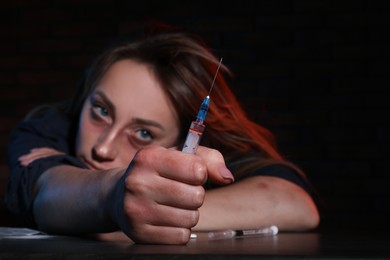Drug addicted woman with syringe at table, focus on hand