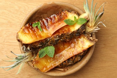 Tasty grilled pineapples in bowl on wooden table, top view
