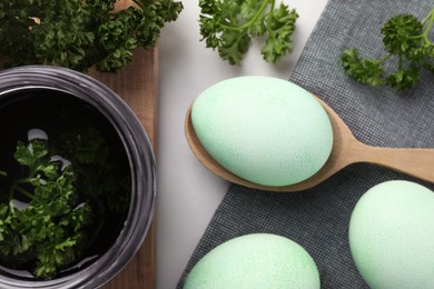Photo of Turquoise Easter eggs painted with natural dye and curly parsley on table, flat lay