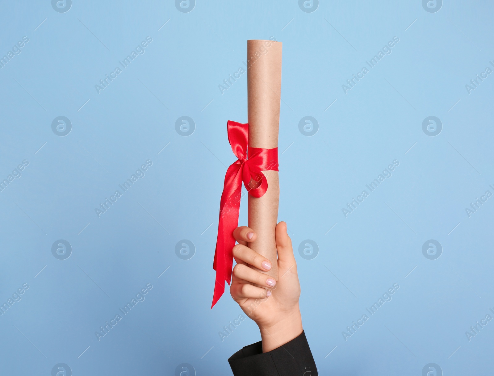 Photo of Student holding rolled diploma with red ribbon on light blue background, closeup