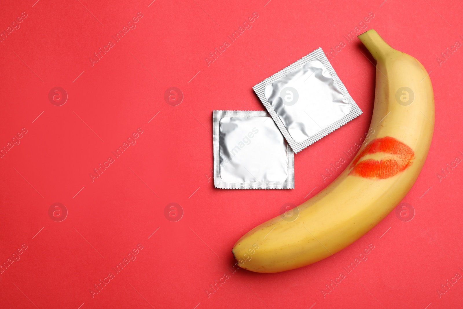 Photo of Condoms, banana with lipstick kiss mark and space for text on red background, flat lay. Safe sex