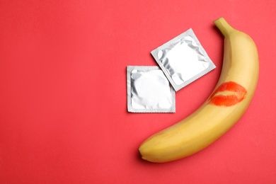 Photo of Condoms, banana with lipstick kiss mark and space for text on red background, flat lay. Safe sex