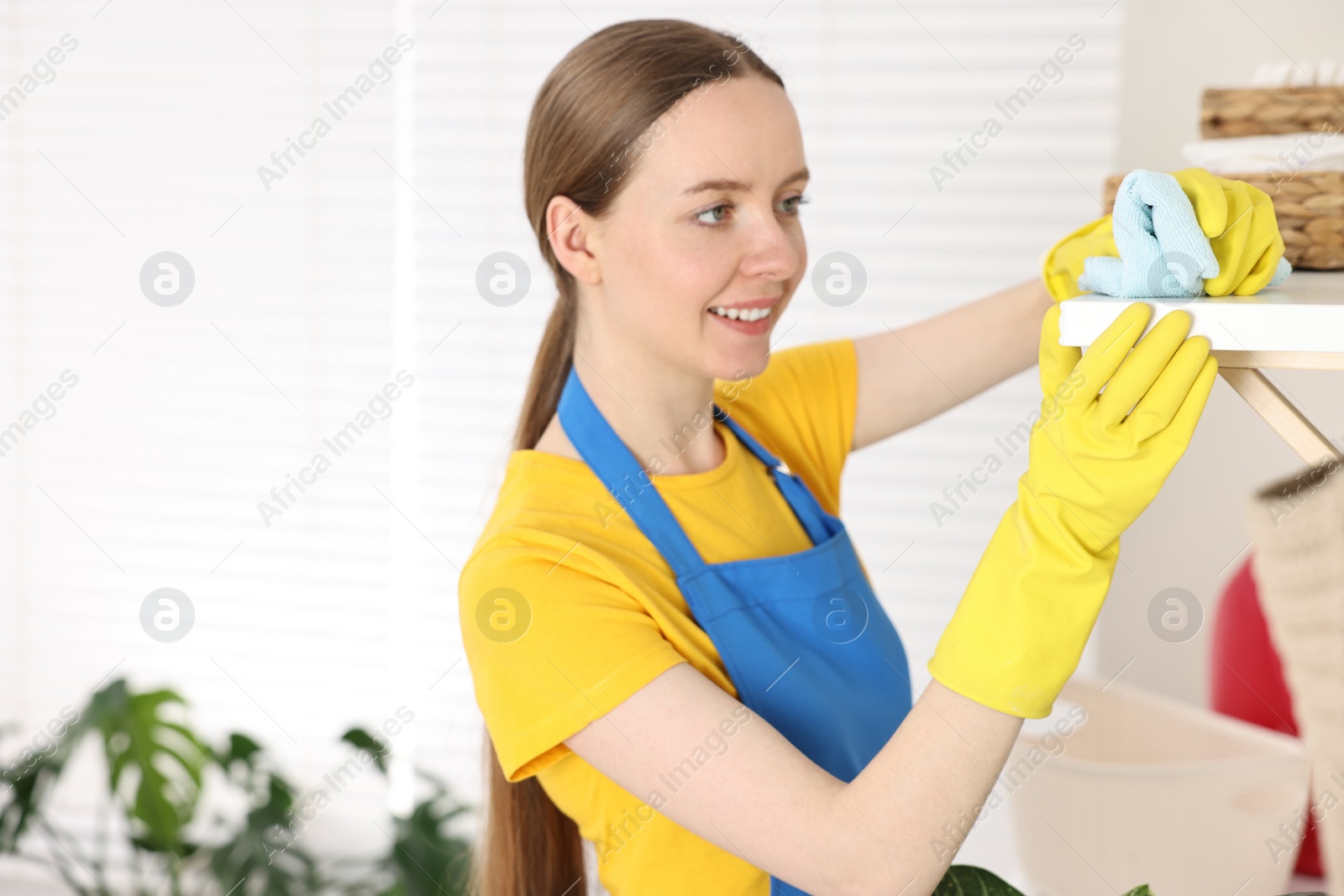 Photo of Woman cleaning shelf with rag at home, space for text