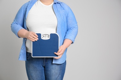 Overweight woman with scales on light background