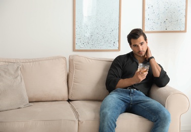 Photo of Young man with glass of whiskey at home. Space for text