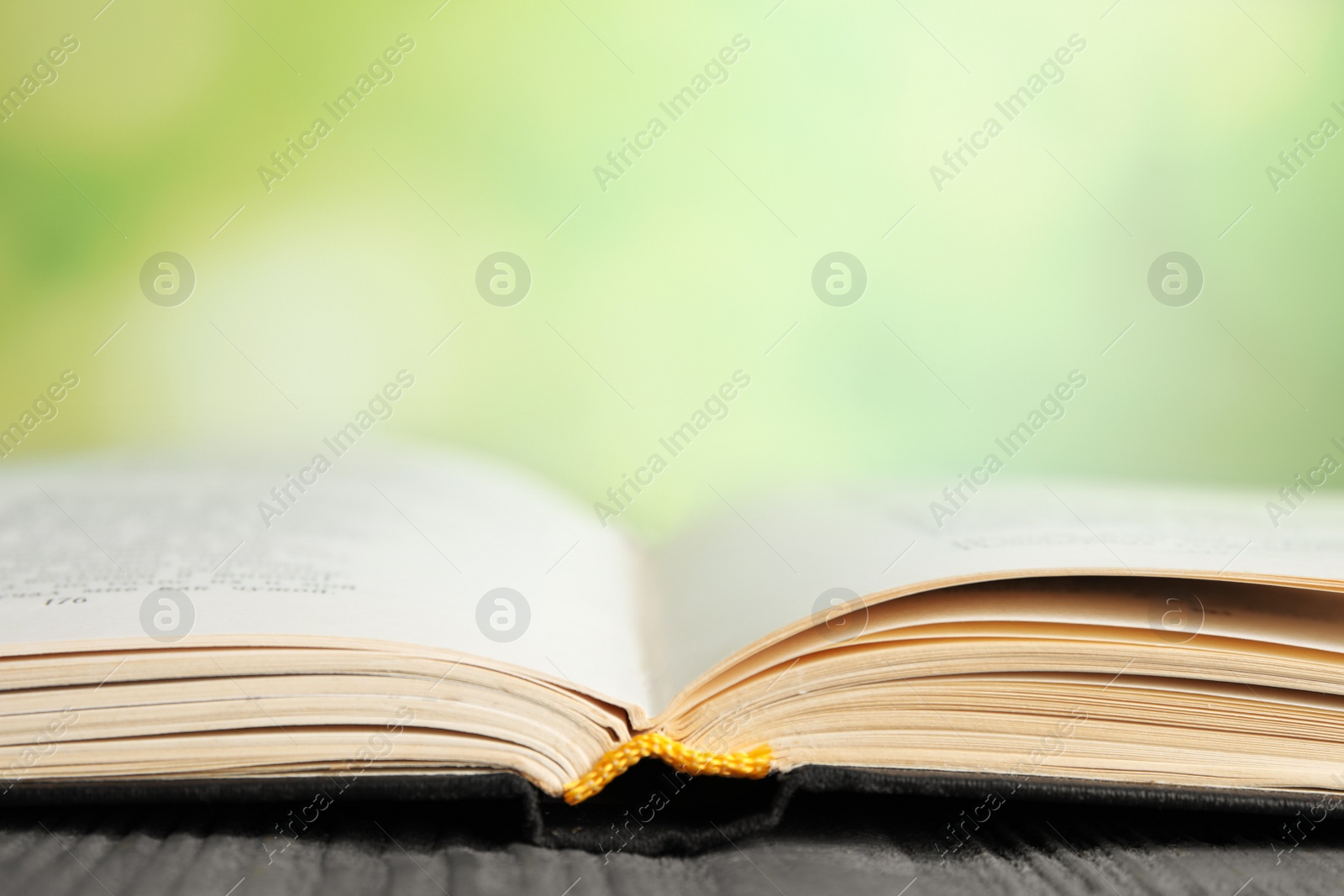 Photo of Open book on blue wooden table against blurred green background, closeup. Space for text