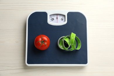 Photo of Scales with tomato and measuring tape on white wooden table, top view. Weight loss