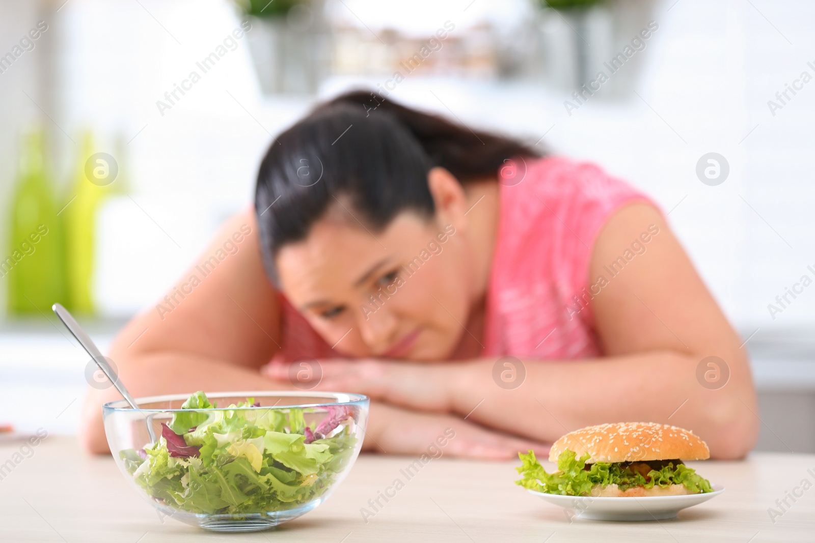 Photo of Salad and burger with blurred overweight woman on background. Healthy diet