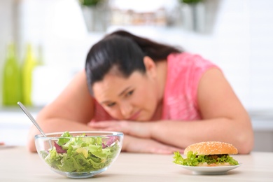 Photo of Salad and burger with blurred overweight woman on background. Healthy diet