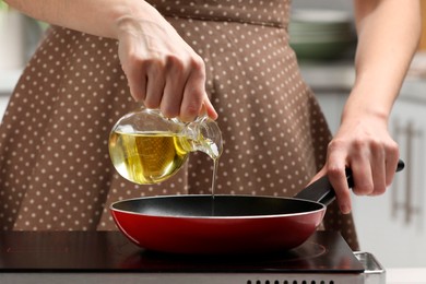 Photo of Vegetable fats. Woman pouring cooking oil into frying pan on stove in kitchen, closeup