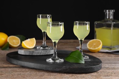 Photo of Tasty limoncello liqueur, lemons and green leaves on wooden table