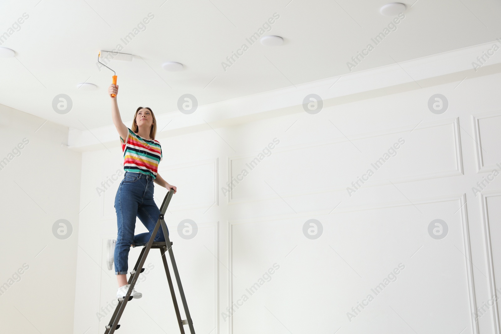 Photo of Young woman painting ceiling with white dye indoors, space for text