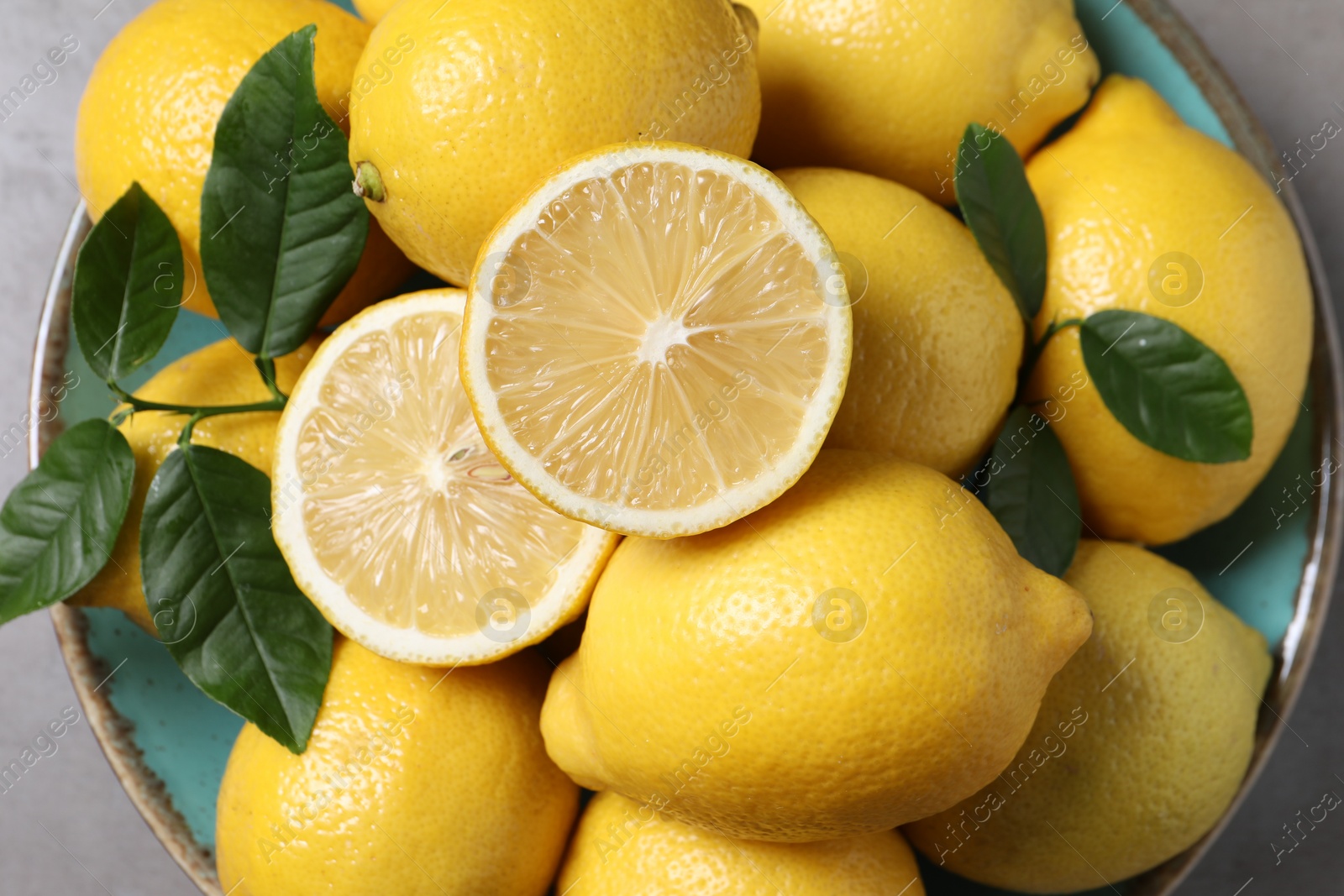 Photo of Fresh lemons and green leaves on grey table, top view