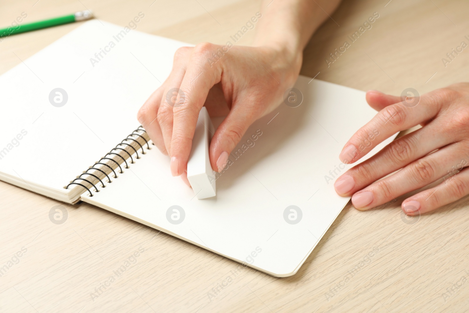 Photo of Woman erasing something in notebook at wooden table, closeup