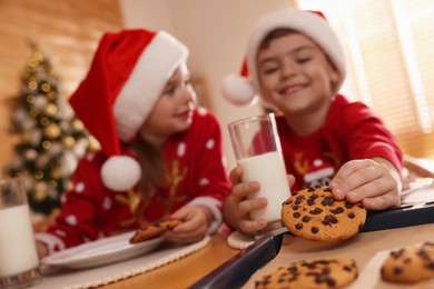 Photo of Cute little children with delicious Christmas cookies and milk at home, focus on pastry