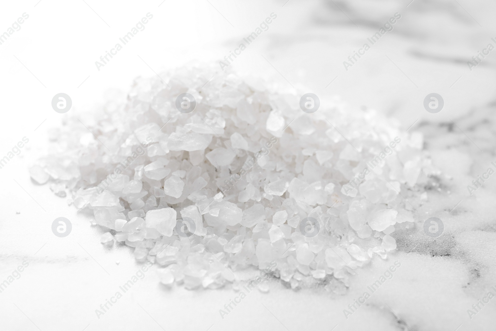 Photo of Pile of white sea salt on marble table, closeup. Spa treatment