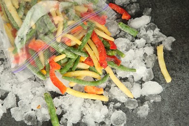 Zip bag with different frozen vegetables and ice on grey table, top view