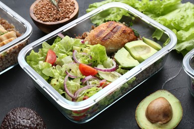 Photo of Healthy meal. Fresh salad, avocado, cutlet and buckwheat in glass container near other products on black table