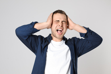 Emotional young man screaming on light background