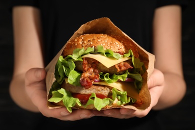 Photo of Woman holding tasty burger with bacon in paper bag, closeup