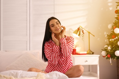 Young woman sitting on bed in room with Christmas tree