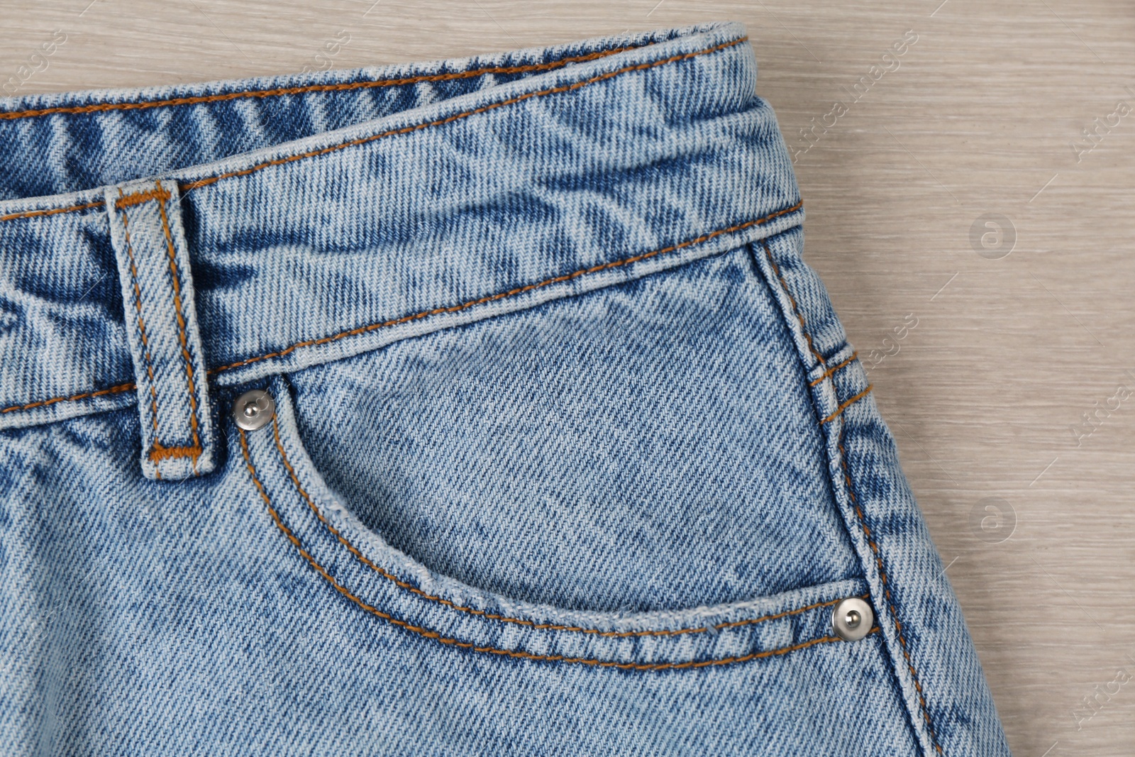 Photo of Stylish light blue jeans on wooden background, closeup of inset pocket