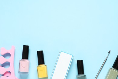 Photo of Nail polishes, toe separators, buffer and cuticle pusher on light blue background, flat lay. Space for text