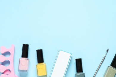 Nail polishes, toe separators, buffer and cuticle pusher on light blue background, flat lay. Space for text