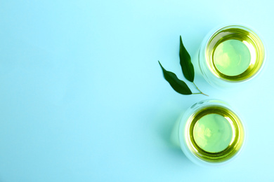 Photo of Aromatic green tea and leaves on light blue background, flat lay. Space for text