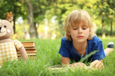 Photo of Cute little boy reading book on green grass in park