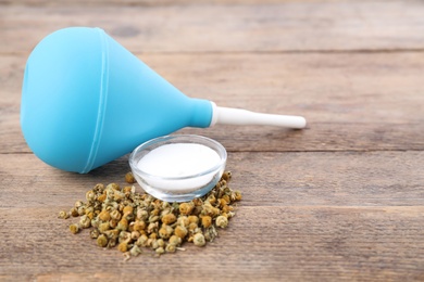 Blue enema, soda powder and dry chamomile flowers on wooden table. Space for text