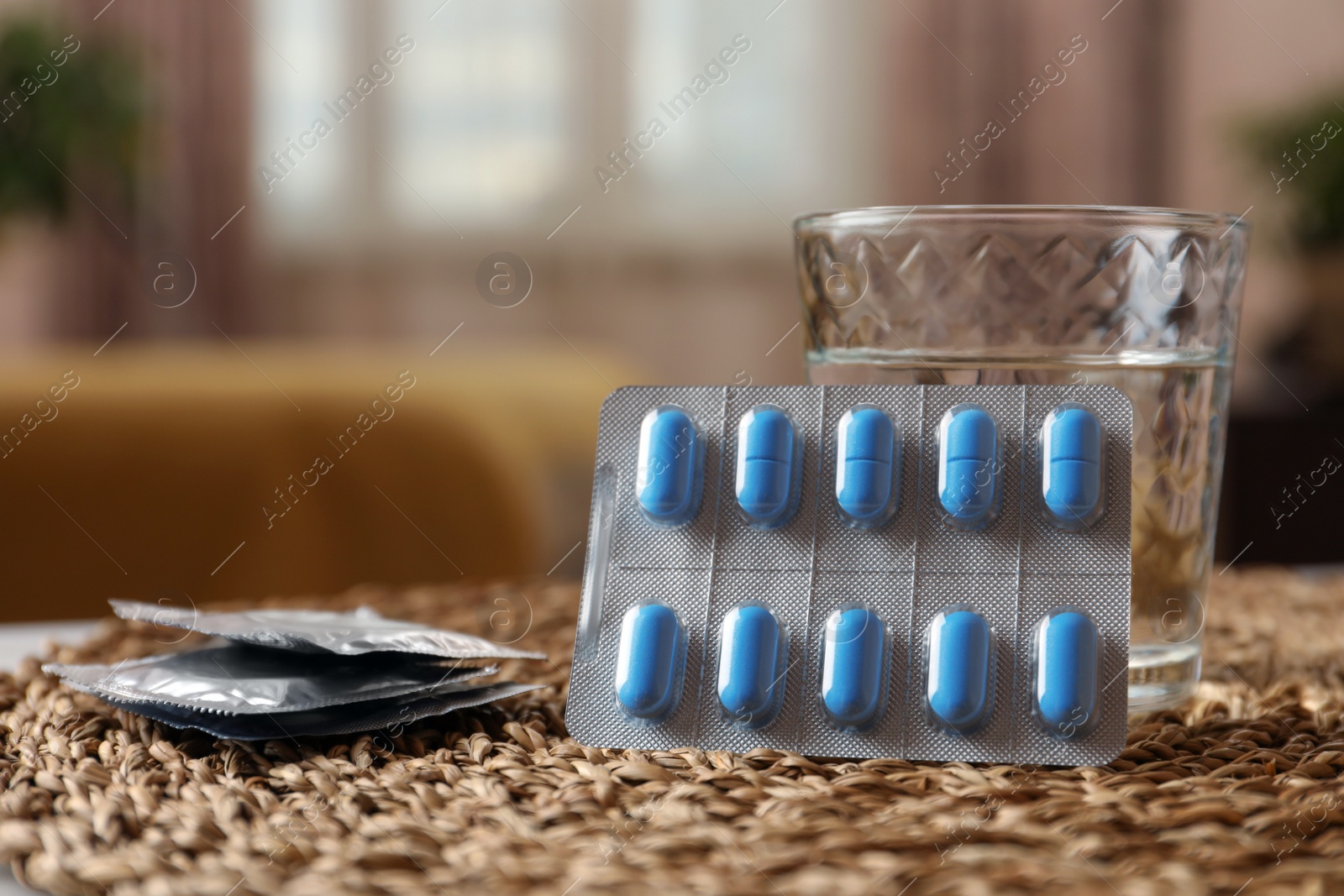 Photo of Glass of water, condoms and pills on wicker mat indoors, space for text. Potency problem concept