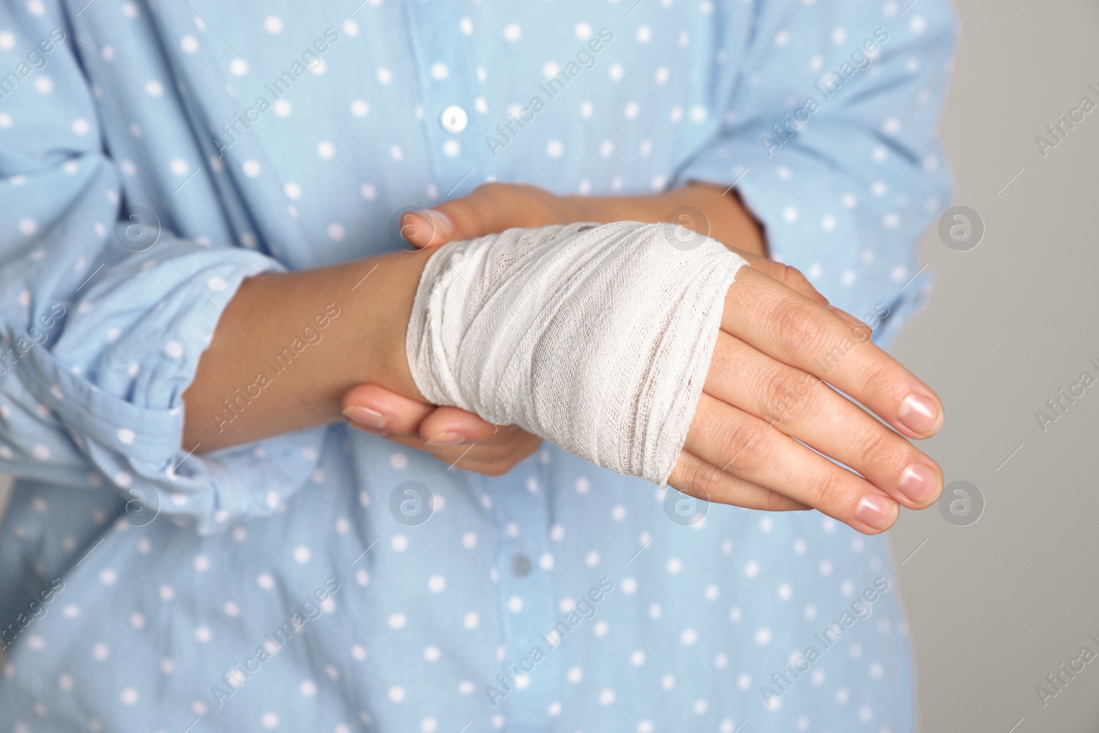 Photo of Woman with hand wrapped in medical bandage on light grey background, closeup