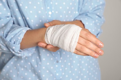 Photo of Woman with hand wrapped in medical bandage on light grey background, closeup