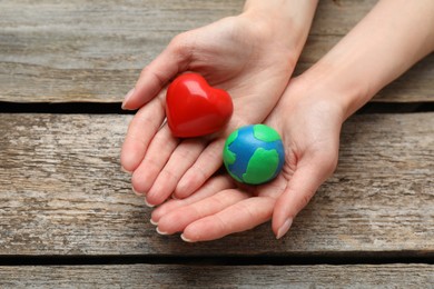 Photo of Happy Earth Day. Woman with plasticine planet and decorative heart at wooden table, closeup