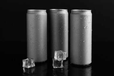 Energy drinks in wet cans and ice cubes on black background