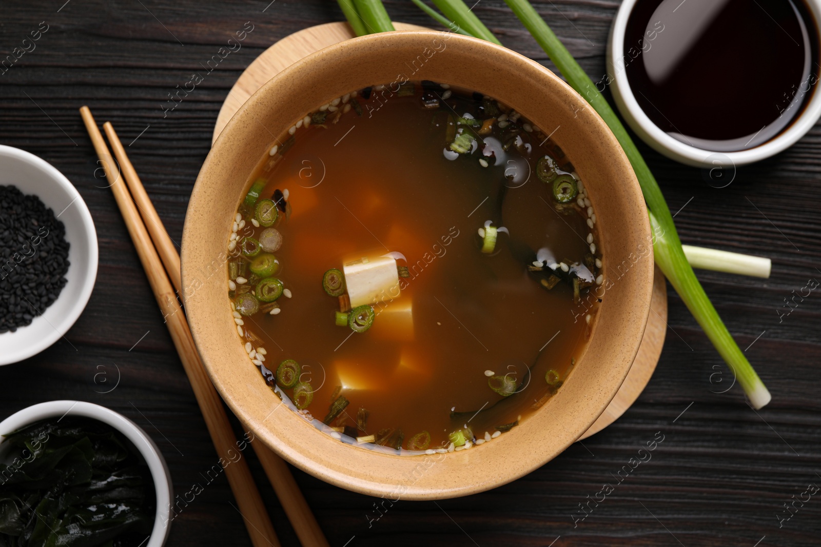 Photo of Bowl of delicious miso soup with tofu served on dark wooden table, flat lay