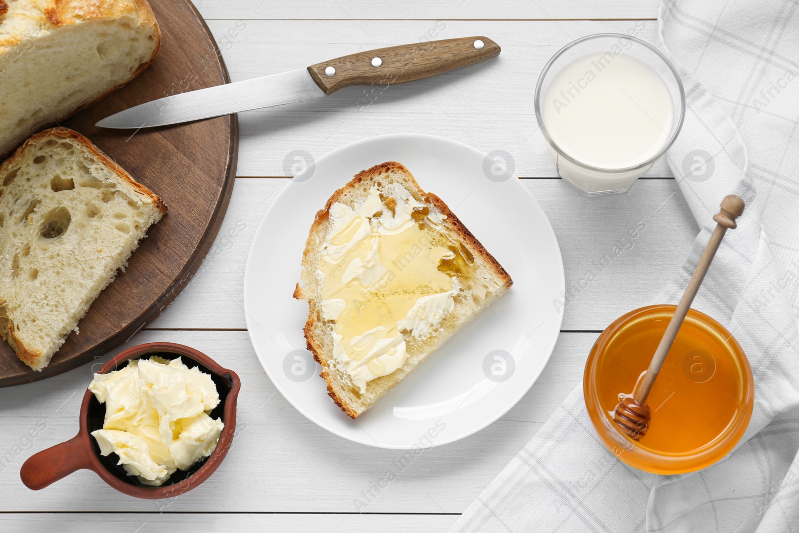 Photo of Glass with fresh milk, honey, butter and bread on white wooden table, flat lay