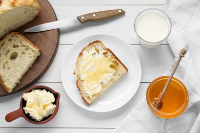 Glass with fresh milk, honey, butter and bread on white wooden table, flat lay