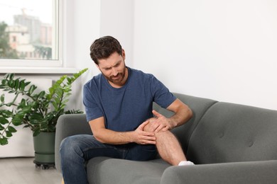Photo of Man suffering from leg pain on sofa at home