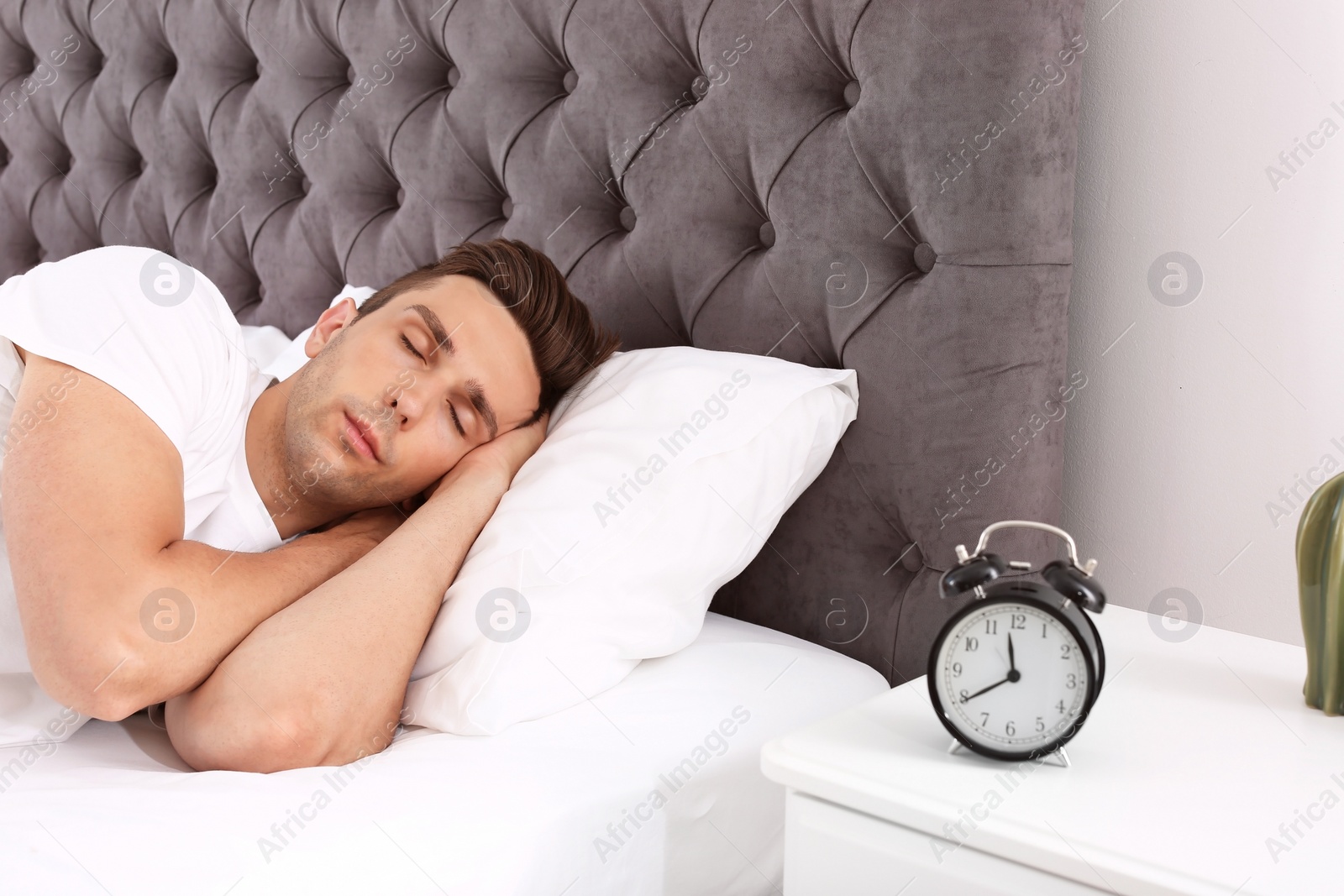 Photo of Young man sleeping in bed and alarm clock on nightstand at home