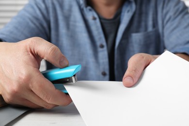 Photo of Man with papers using stapler at white table, closeup