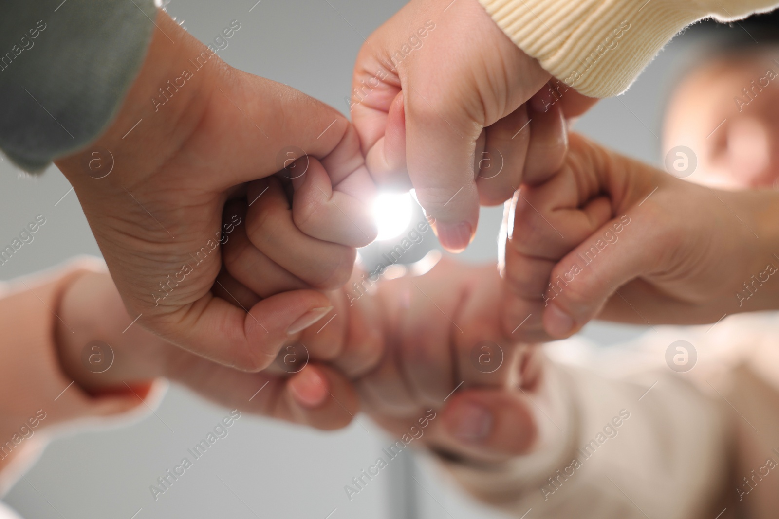 Photo of Group of people holding fists together indoors, low angle view. Unity concept