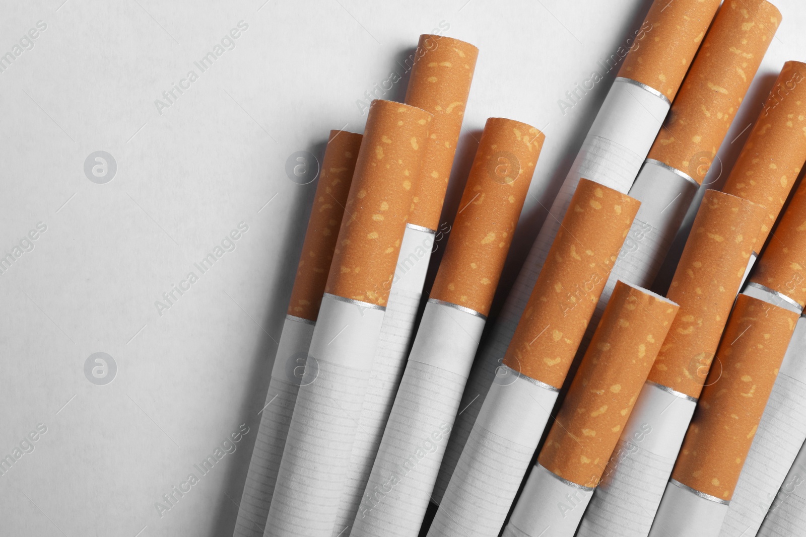 Photo of Pile of cigarettes with orange filters on white background, flat lay