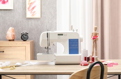 Photo of White sewing machine, cloth, craft accessories and mannequin on wooden table indoors