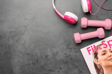 Photo of Dumbbells, headphones and magazine on brown textured table, flat lay. Space for text