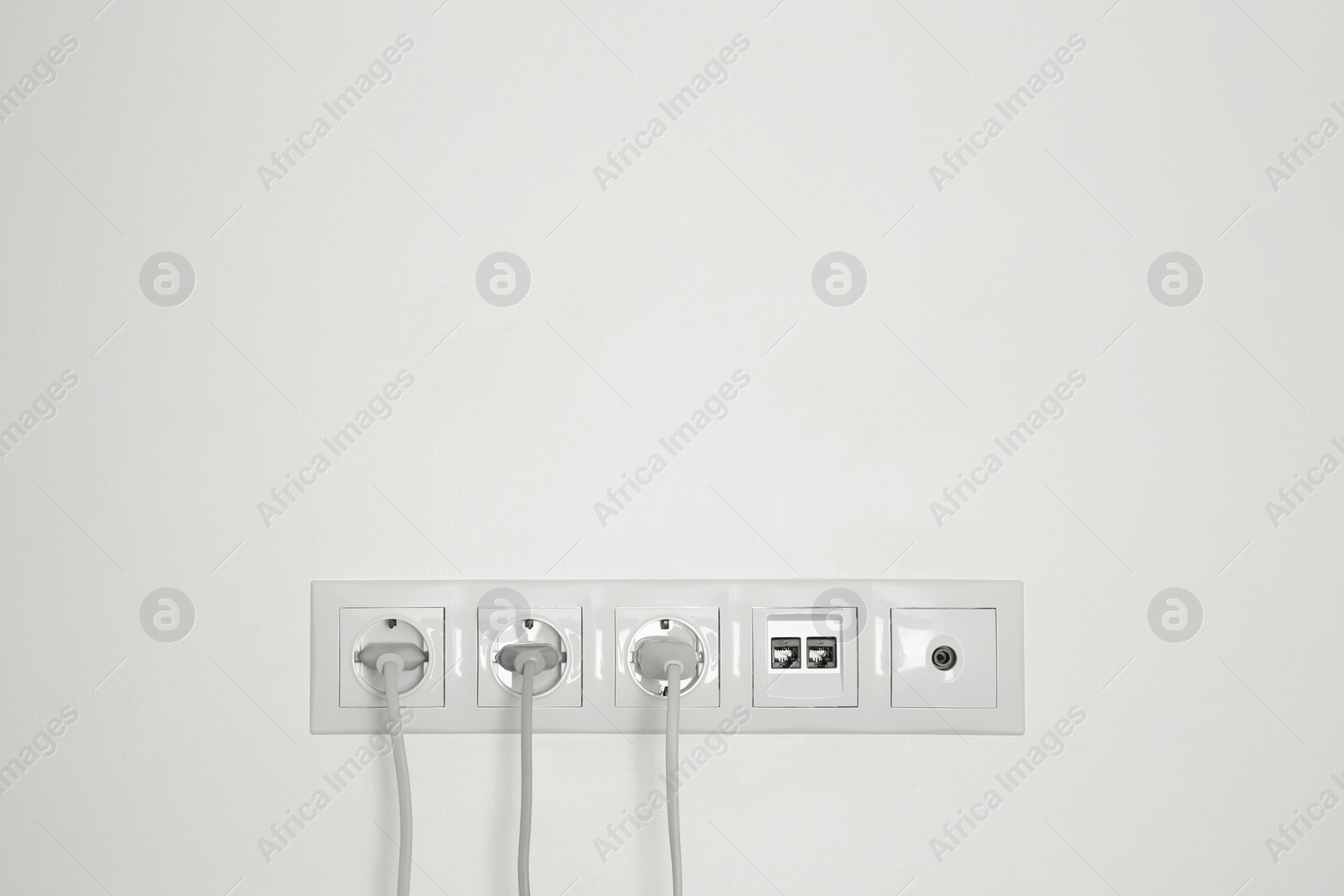 Photo of Many power sockets with plugs, ethernet and TV coax plates on white wall indoors. Space for text