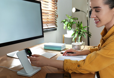 Photo of Woman at desk and watch on wireless charger. Modern workplace